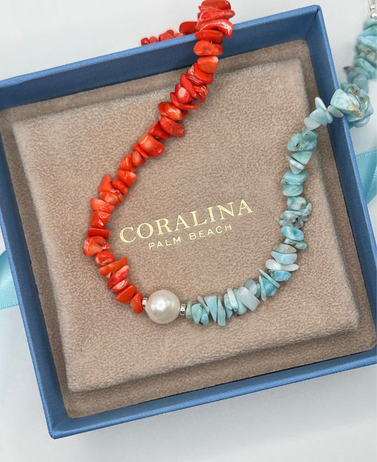 A red coral and blue Larimar necklace offset by a large white baroque pearl and finished with 925 sterling silver. The necklace is sitting in a custom Italian Coralina Palm Beach box. 