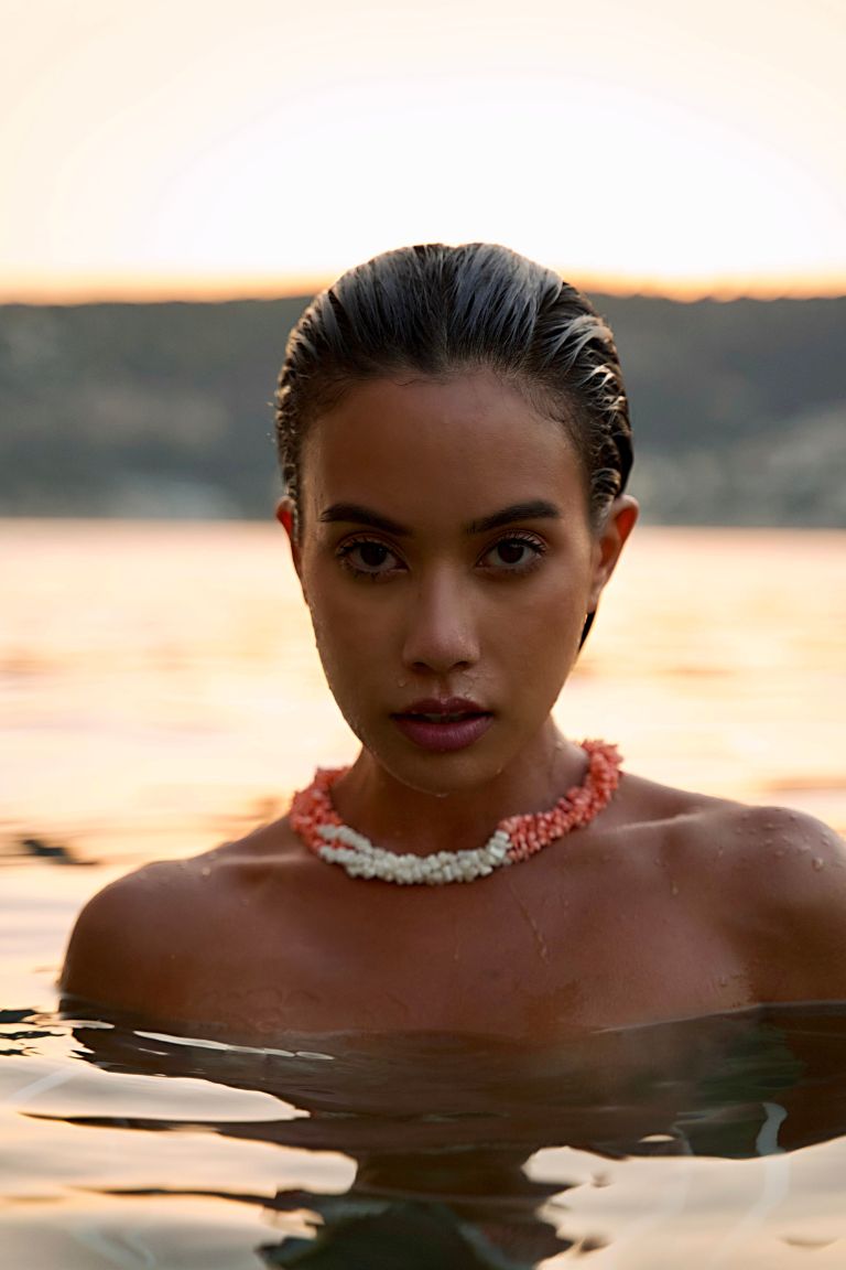 Girl in the water wearing a triple strand necklace of pastel pink/peach and bright white coral twisted and finished with sterling silver. 