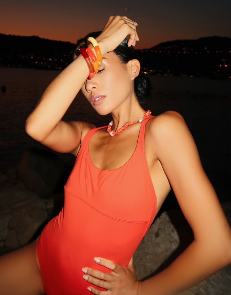 Girl wearing three red, orange and yellow resin bracelets with a coral and pearl necklace. 